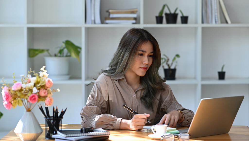A woman seated at a table, focused on her laptop, engaged in work or study.
