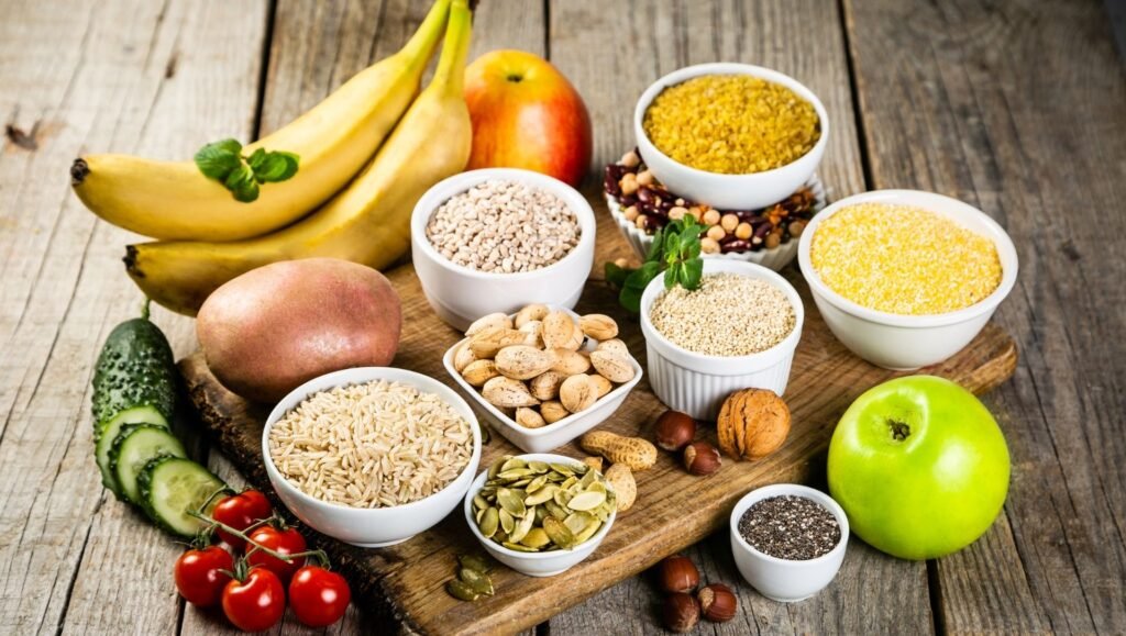 Assortment of whole grains, seeds, nuts, fruits, and vegetables on a rustic wooden surface.